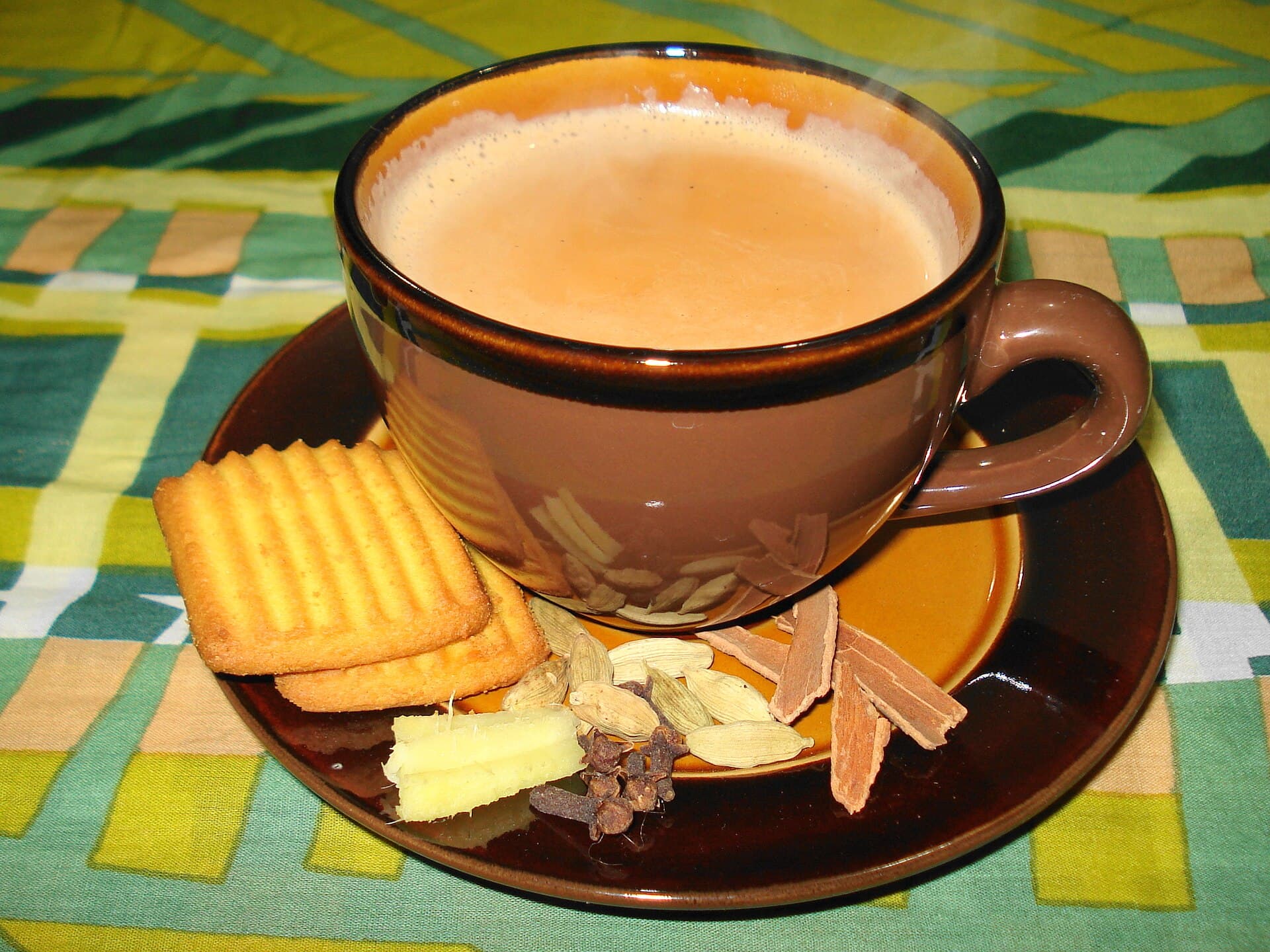 A cup of masala chai with biscuits and whole spices