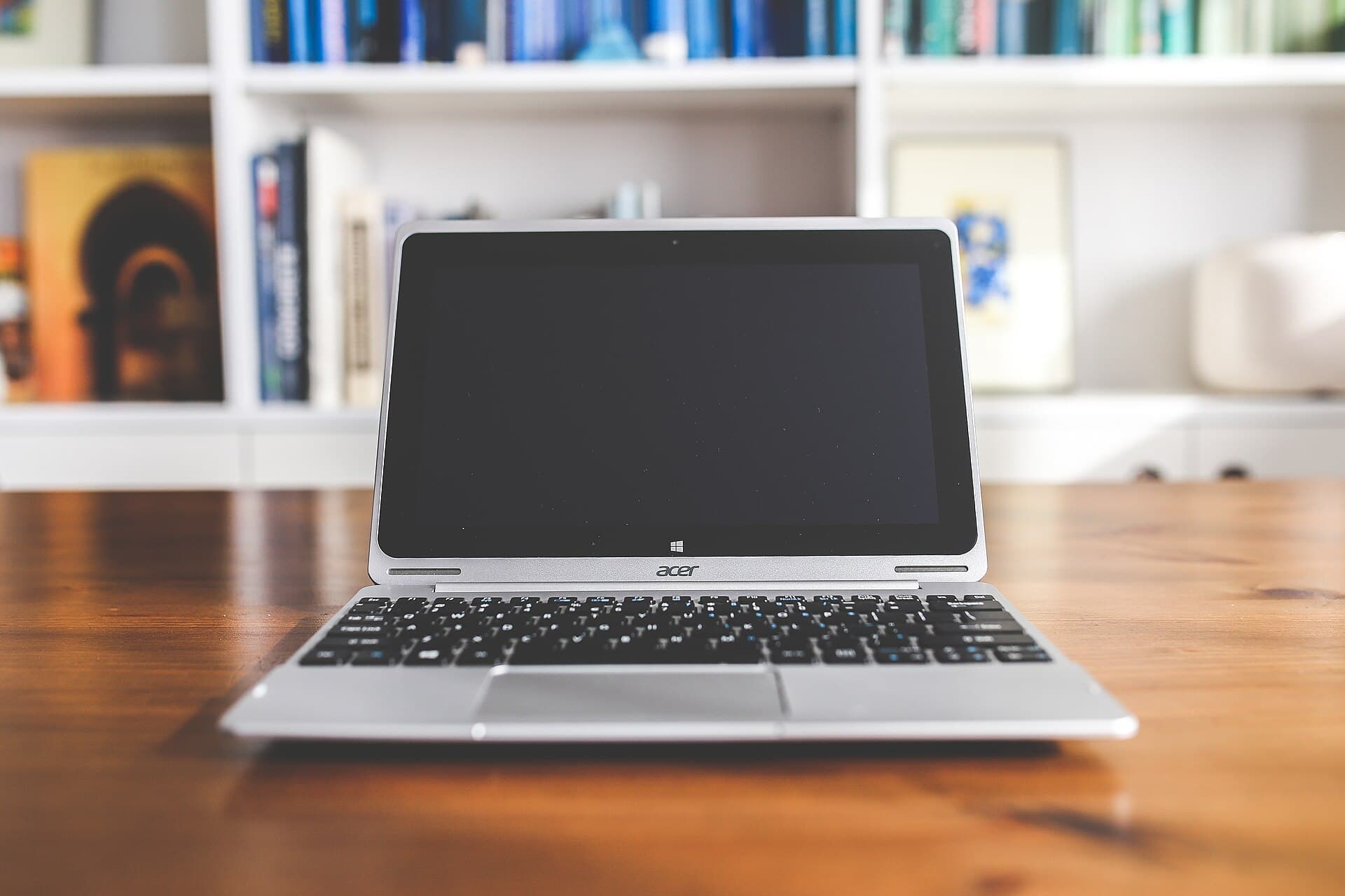 A laptop on a wooden desk in front of a bookshelf