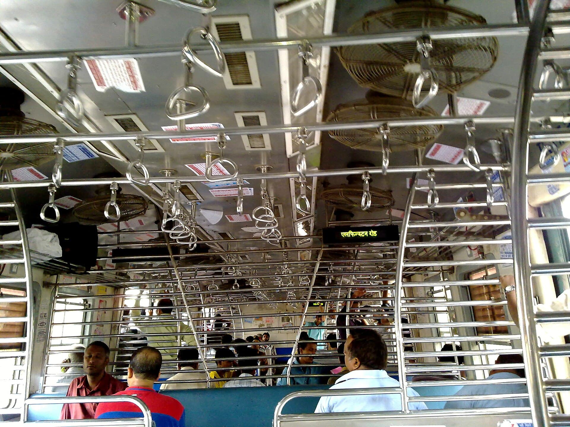 Inside a Mumbai local train carriage, rows of hand grips over passengers