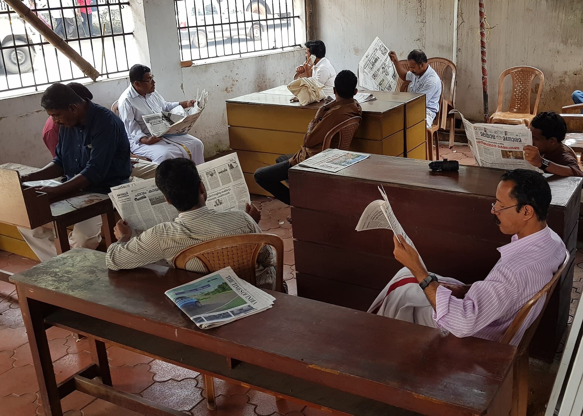 Readers at long wooden tables in the open reading room of a public library in Kannur